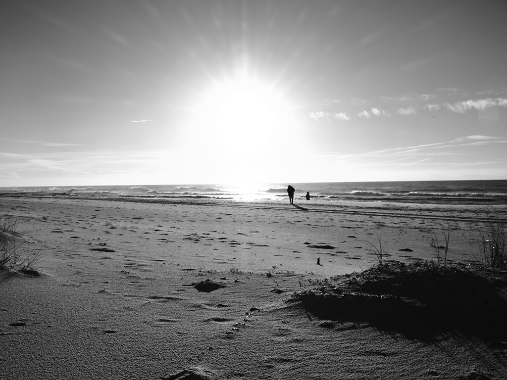 Black and White photography of people walking along the beach