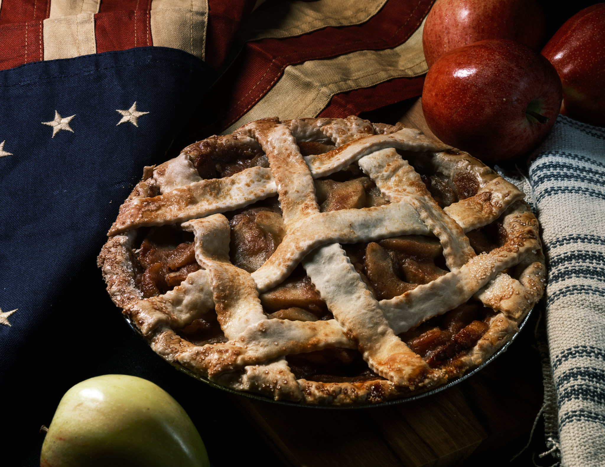 Still-life photography of an apple pie, colonial flag, and flowers